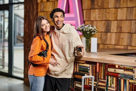 happy diverse couple, dressed in casual clothes standing happily surrounded by shelves of books