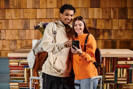 Diverse glückliche Paar teilen Moment der Freude, während sie durch digitale Bibliothek auf dem Smartphone blättern