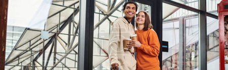 Photo for Young diverse couple smiling while holding coffee to go and entering a modern hostel, banner - Royalty Free Image