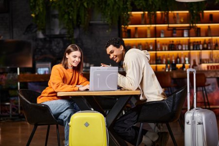 Schwarze Männer und Frauen schauen auf Laptop auf Cafétisch, ihr Gepäck neben sich, reisen