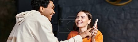 happy woman in orange sweater shows  phone to smiling black boyfriend while sitting in cafe, banner