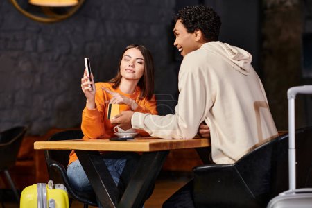 black man holding credit card while his girlfriend using smartphone near coffee cups in cafe