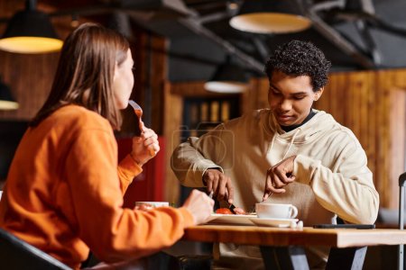 Téléchargez les photos : Couple jeune et diversifié dégustant un délicieux déjeuner à une table en bois rustique dans un charmant restaurant - en image libre de droit