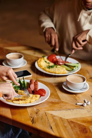 young diverse couple enjoying breakfast in cafe, omelette,  and sausages near cup of coffee