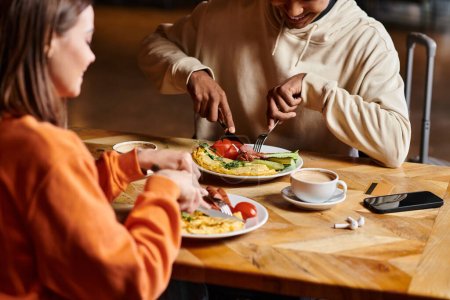 Vielseitiges Paar genießt Frühstück mit leckerem Omelett und Würstchen in der Nähe von Tassen Kaffee