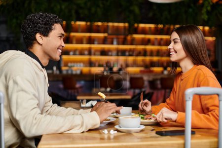Téléchargez les photos : Heureux couple diversifié profiter d'un délicieux repas dans l'ambiance charmante d'un restaurant intérieur - en image libre de droit