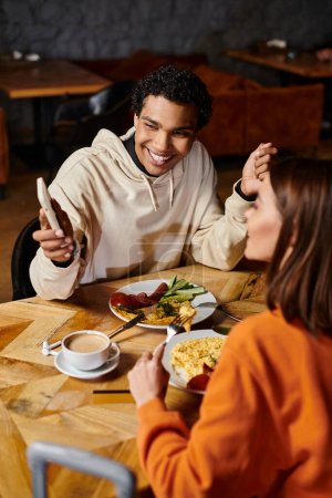 Ein Paar genießt ein gemütliches Essen zusammen, schwarzer Mann zeigt Freundin Smartphone