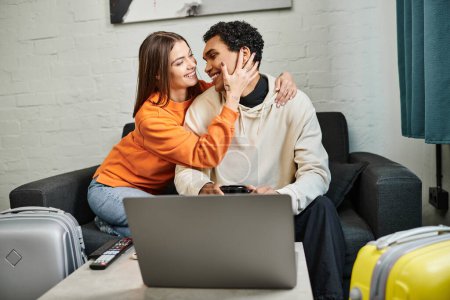 Smiling diverse couple sitting on sofa, woman touching face of black boyfriend