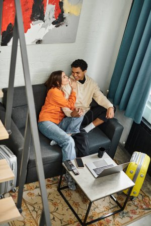 Diverse liebevolle Paar gefangen in Moment der spielerischen Unterhaltung auf bequemen Couch, Reisekonzept