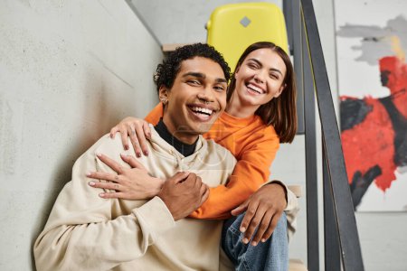 cheerful interracial couple in casual attire against a backdrop of a brick wall in hostel