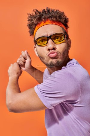 aktiver junger afrikanisch-amerikanischer Mann gestikuliert und schmollende Lippen auf orangefarbenem Hintergrund, dynamisch