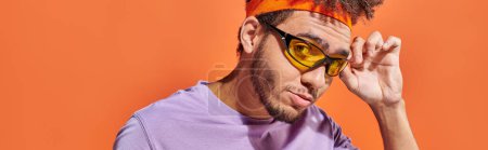 Téléchargez les photos : Bannière, jeune homme afro-américain ajustant les lunettes de soleil et regardant la caméra sur fond orange - en image libre de droit