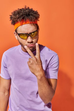 ernster Gesichtsausdruck, junger afrikanisch-amerikanischer Mann macht Augenkontakt-Geste auf orangefarbenem Hintergrund