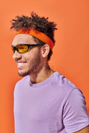Téléchargez les photos : Heureux Afro-Américain dans les lunettes regardant loin sur fond orange, homme optimiste - en image libre de droit