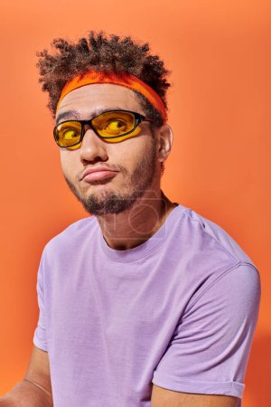 Photo for Confused african american fella in eyeglasses and headband looking away on orange background - Royalty Free Image