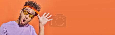 banner, african american man with surprised face expression adjusting headband on orange background
