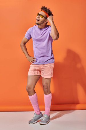 thoughtful african american sportsman in sunglasses and gym attire thinking on orange background