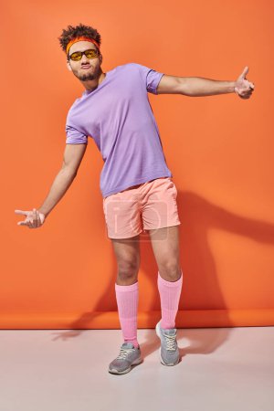cool african american sportsman in gym attire and sunglasses gesturing on orange background