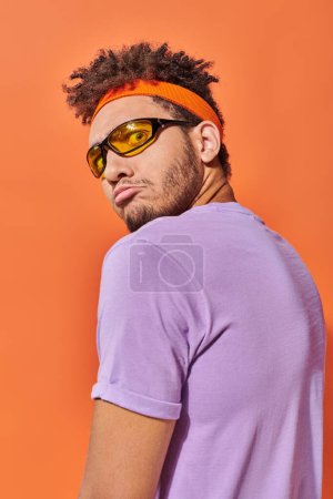 Afrikanisch-amerikanischer Mann mit Brille blickt mit weit geöffneten Augen auf orangefarbenem Hintergrund in die Kamera