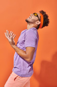 expressive african american man in eyeglasses and headband screaming on orange background, gesture t-shirt #692584846