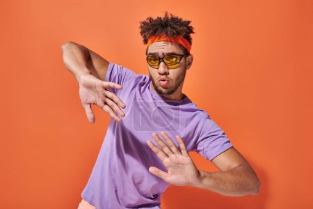 ausdrucksstarker afrikanisch-amerikanischer Mann mit Brille und Stirnband gestikuliert auf orangefarbenem Hintergrund