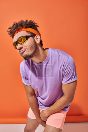 Photo for Funny african american man in eyeglasses and headband pouting lips on orange background - Royalty Free Image