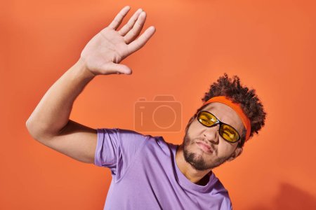 Photo for African american man in eyeglasses pouting lips and covering face from light on orange background - Royalty Free Image
