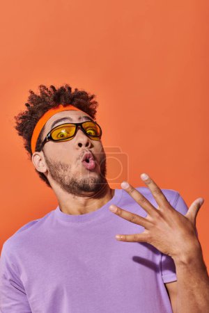 Photo for Surprised african american man in eyeglasses and headband looking at camera on orange background - Royalty Free Image