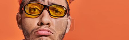 Téléchargez les photos : Homme afro-américain bouleversé dans les lunettes et bandeau sourire sur fond orange, bannière grimace - en image libre de droit