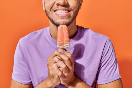 cropped shot of african american man holding ice cream with sprinkles on orange background