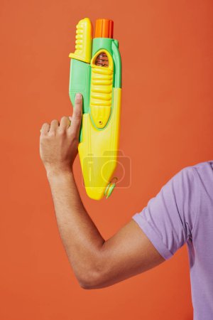 cropped photo of african american man playing water fight with toy gun on orange background