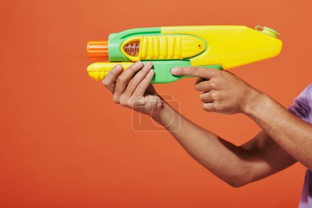 Schnappschuss eines afrikanisch-amerikanischen Mannes, der mit einer Spielzeugpistole auf orangefarbenem Hintergrund eine Wasserschlacht spielt