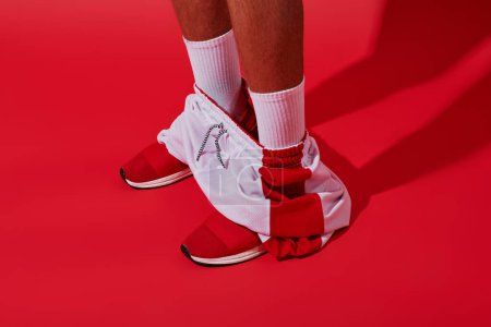 foto conceptual, hombre recortado en zapatillas de deporte, calcetines blancos y corredores de pie sobre fondo rojo