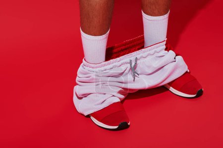 Modefotografie, beschnittener Mann in Turnschuhen, weißen Socken und Joggern auf rotem Hintergrund
