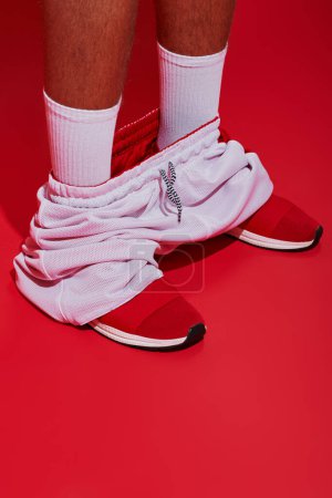 Foto de Fotografía de moda, chico recortado en zapatillas de deporte, calcetines blancos y corredores de pie sobre fondo rojo - Imagen libre de derechos