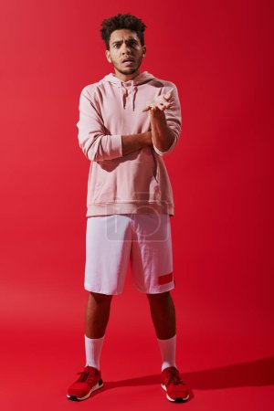 ernster afrikanisch-amerikanischer Sportler in Turnbekleidung gestikuliert, während er sich auf rotem Hintergrund beschwert