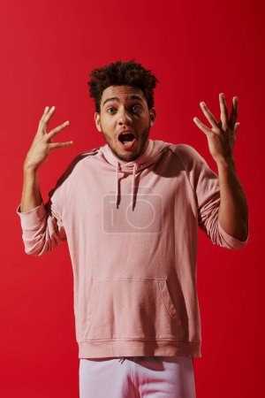 Foto de Hombre afroamericano confuso en ropa de gimnasio gesto con la boca abierta sobre fondo rojo - Imagen libre de derechos