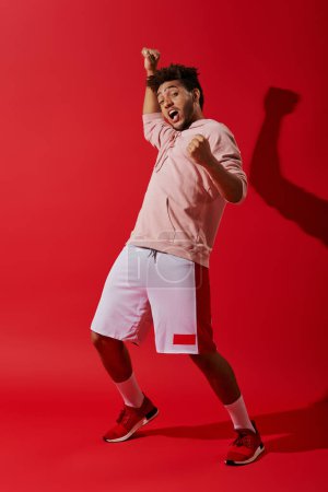aufgeregter afrikanisch-amerikanischer Mann in Sportbekleidung jubelt und blickt in die Kamera auf rotem Hintergrund