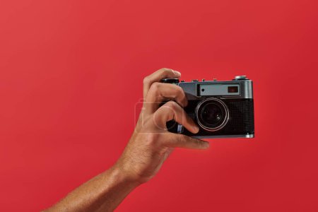cropped view of african american photographer taking shot on retro camera on red background