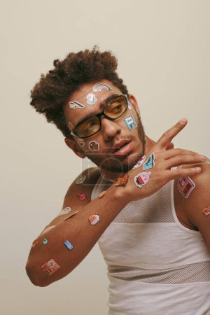 young african american guy in sunglasses with stickers on face gesturing on grey background