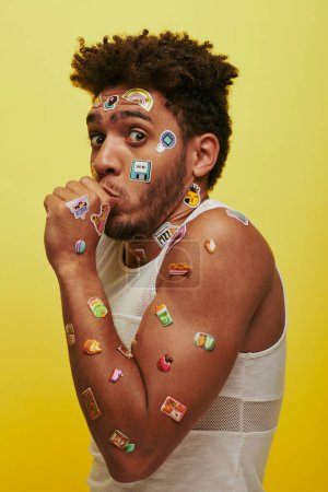 shocked african american guy in tank top with stickers on face looking at camera on green backdrop