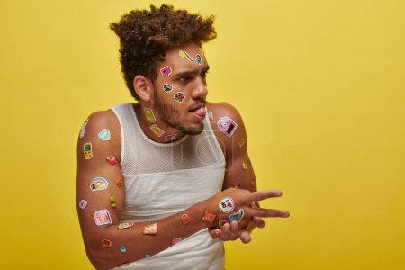 funny african american guy in tank top with stickers on face sticking out tongue on green backdrop