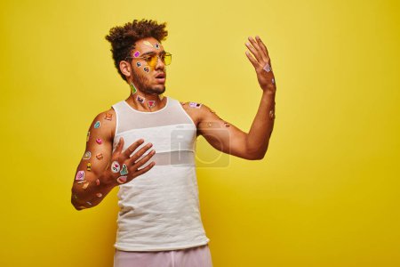 surprised african american man looking at stickers on his hands and body on yellow background