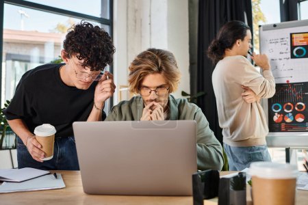 Männer in ihren Zwanzigern werten Startup-Daten am Laptop aus, während Mitarbeiter im Hintergrund Diagramme betrachten