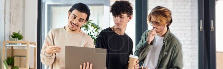 Three young men engaged in a lively discussion over a laptop at a coworking space, startup banner