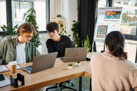 Jeunes professionnels dans la vingtaine partageant des idées près d'ordinateurs portables dans un espace de coworking, au premier plan flou