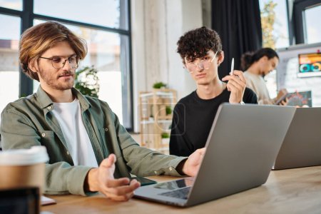 Junges Start-up-Team arbeitet konzentriert an Laptops im modernen Coworking Space, Männer in den 20er Jahren