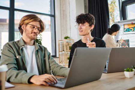 Junges Start-up-Team diskutiert Projekt während der Arbeit an Laptops in einem Coworking Space, Männer in den 20ern