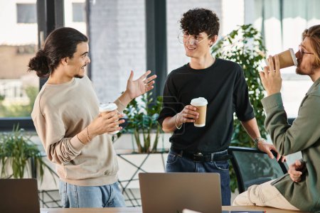 friendly conversation between three young coworkers holding coffee to go in modern office, startup