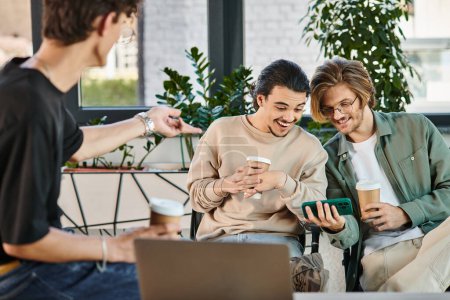 Téléchargez les photos : Jeunes hommes joyeux bavarder pendant la pause café au bureau et regarder la vidéo sur smartphone - en image libre de droit